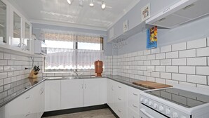 A kitchen with white cabinets, a wooden countertop, a stove, and a window with a floral curtain. - Berdella 34 - Flynn's Beach (Port Macquarie)
