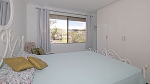 A bedroom with a bed, a window with curtains, a wardrobe, and a mirror. - Berdella 34 - Flynn's Beach (Port Macquarie)