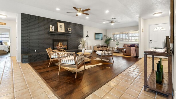 A spacious living room with a dark brick fireplace, wooden flooring, and wicker furniture.