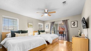 A bedroom with two beds, a ceiling fan, a wooden cabinet, and artwork on the walls.