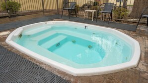 Ett rektangulärt bubbelbad med vit insida och blå utsida, omgivet av en stenbelagd uteplats.