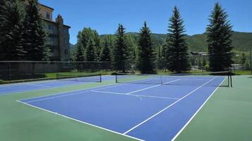 Tenniskenttä, jossa on verkko, ja jonka ympärillä on puita ja rakennuksia.