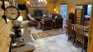L’intérieur chaleureux d’un chalet en bois comprend une cheminée, des meubles en cuir, une horloge et un coin repas.