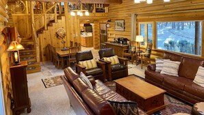 L’intérieur d’une cabane en rondins comprend un coin repas, une cuisine et un espace détente avec vue sur la forêt.