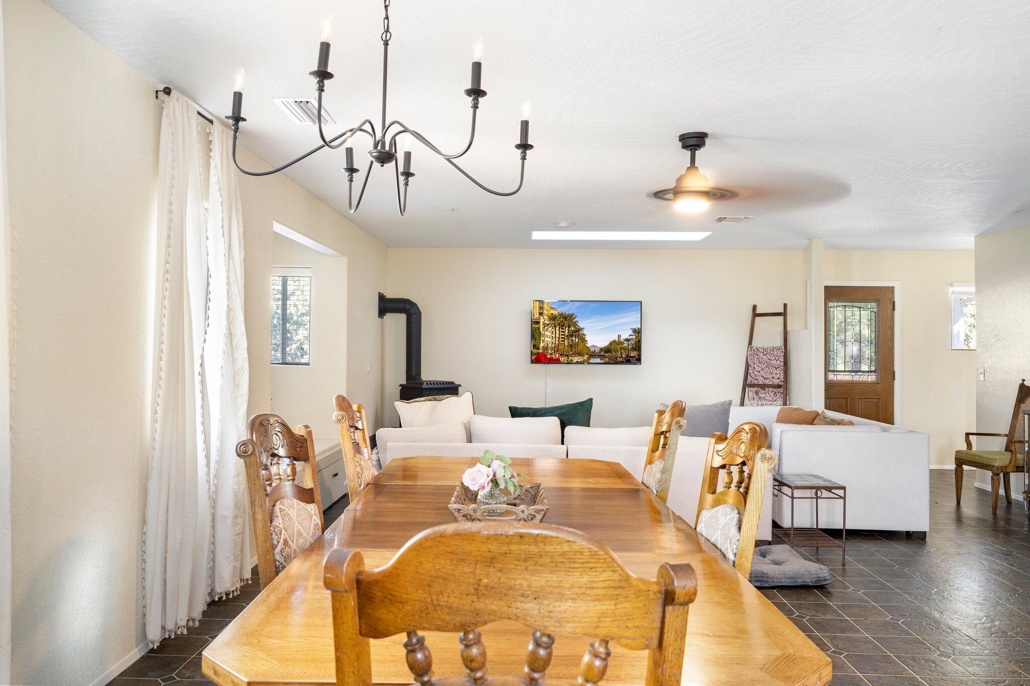 A dining room with a wooden table, chairs, a chandelier, and a painting on the wall.
