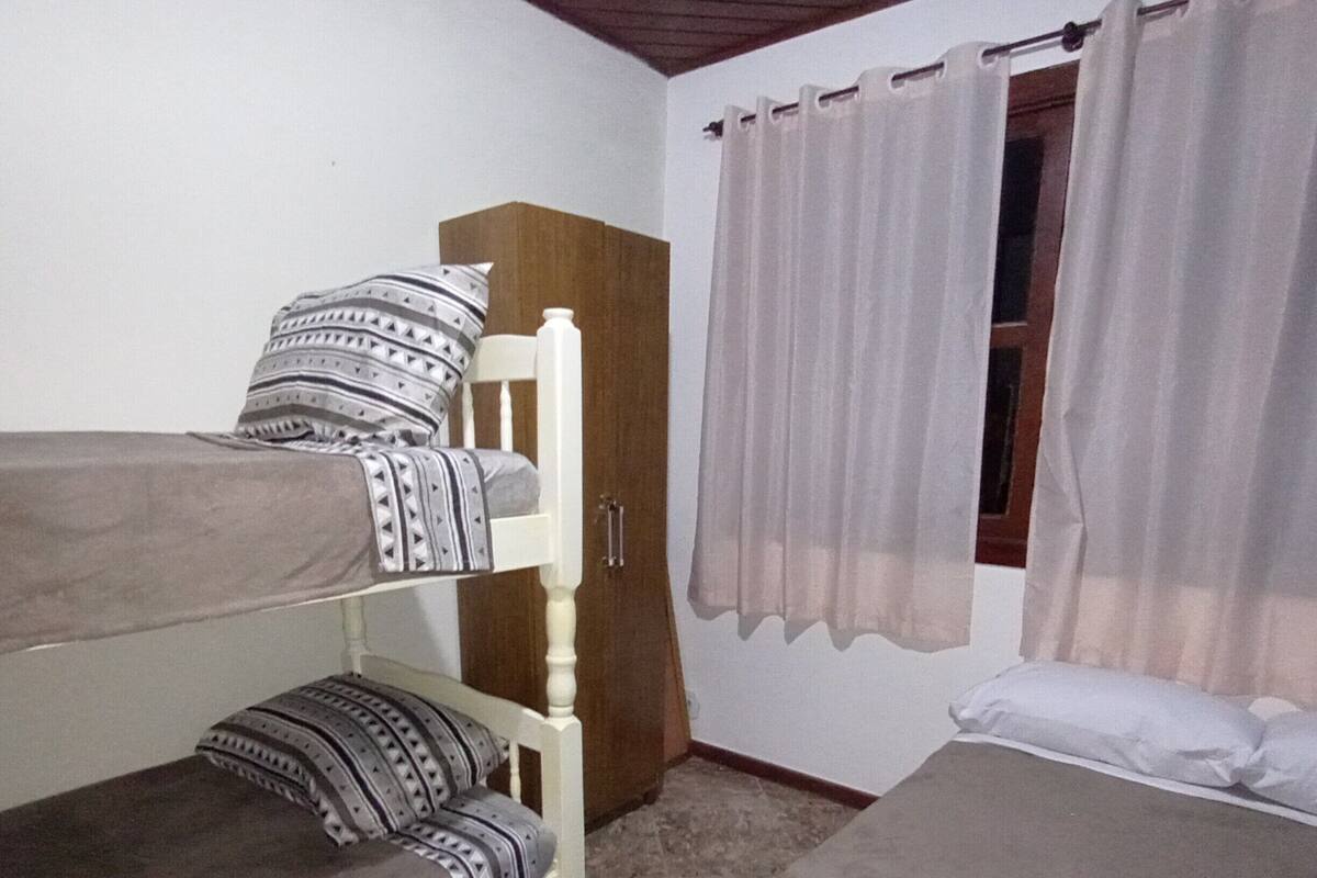 A dormitory room with bunk beds, a wardrobe, and a window with curtains.