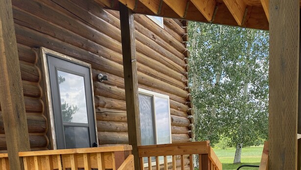 Eine Holzhütte mit einer Veranda, einer Bank und einer Tür.