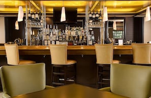 Zona de bar con varios taburetes y una barra repleta de botellas.