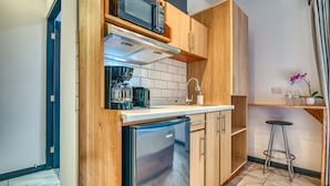 Une cuisine compacte avec des meubles en bois, un four à micro-ondes encastré, un réfrigérateur en acier inoxydable et un petit tabouret de bar.