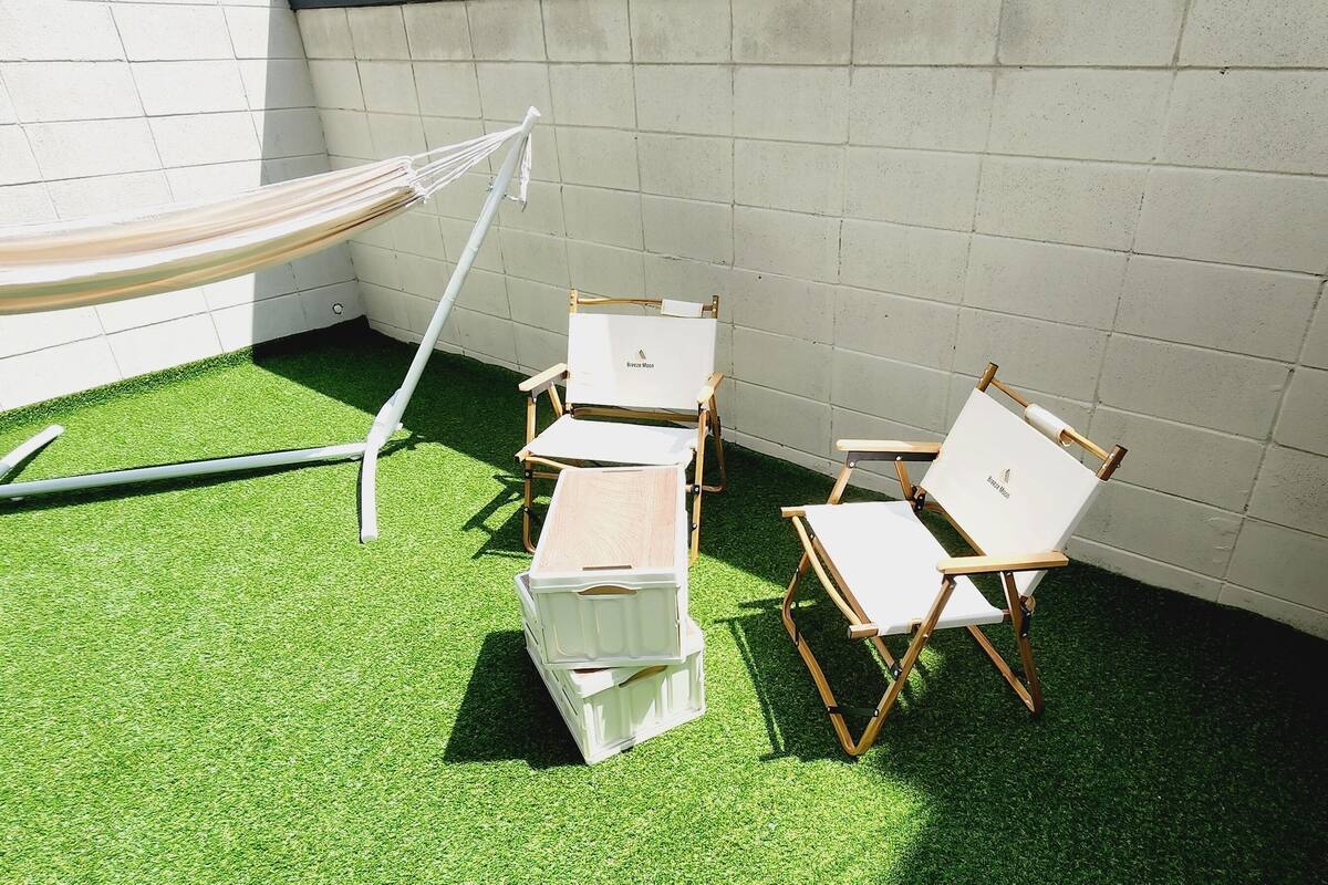 A small outdoor area with artificial green turf, a hammock, and a set of wooden folding chairs.