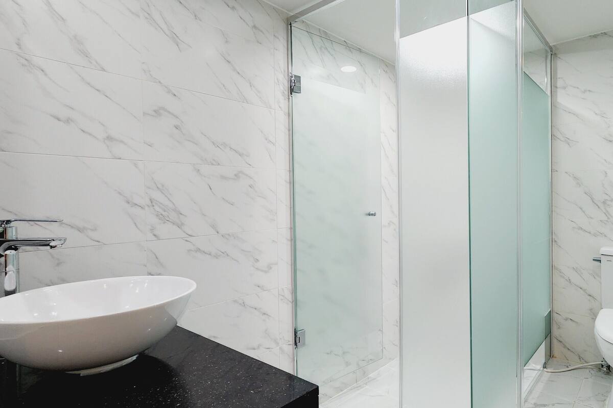 A modern bathroom with a marble floor, a white sink, a glass shower enclosure, and a toilet.