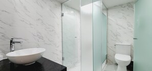 A modern bathroom with a marble floor, a white sink, a glass shower enclosure, and a toilet.