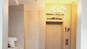A modern elevator with a chandelier, a clean floor, and a visible floor number '1F'. - DAON HOTEL (Gimhae)