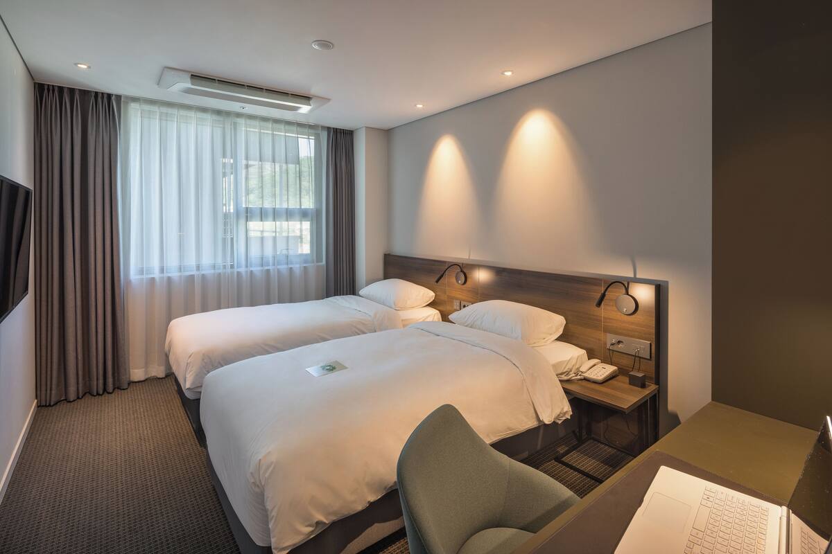 Habitación de hotel con dos camas, un escritorio con silla, un teléfono y una lámpara de pared.