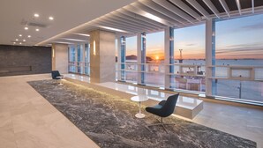 A spacious lobby with a modern design, featuring a large window with a view of the sunset, a marble floor, and contemporary seating. - Grab the Ocean SONGDO (Busan)