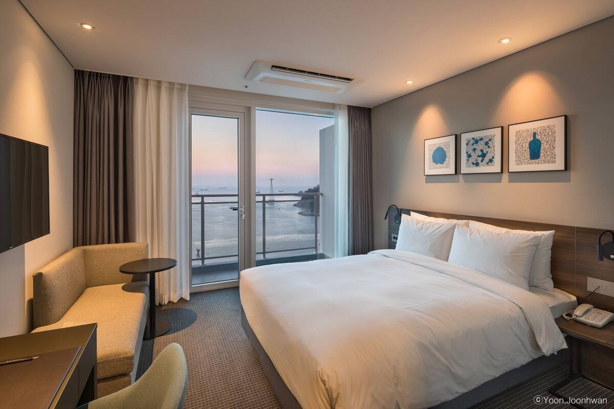 Habitación de hotel con una cama grande, un escritorio, una silla, un televisor y un balcón con vista al mar.