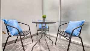 Eine Sitzecke mit zwei Stühlen und einem kleinen Tisch, jeweils mit einem blauen Kissen. Auf dem Tisch steht ein kleiner Blumentopf.
