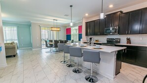 A modern kitchen with dark cabinets, a white island, and bar stools. -  6 Br/5 Ba Pool/Game /Themed Handpainting Villa (Kissimmee)
