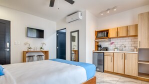Een moderne slaapkamer met een groot bed, een televisie en een kitchenette met houten kastjes en een magnetron.