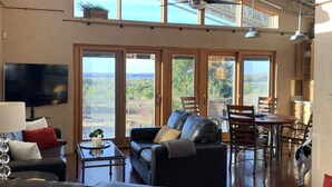 A spacious living area with a large black leather sofa, a dining table with chairs, and a TV mounted on the wall.