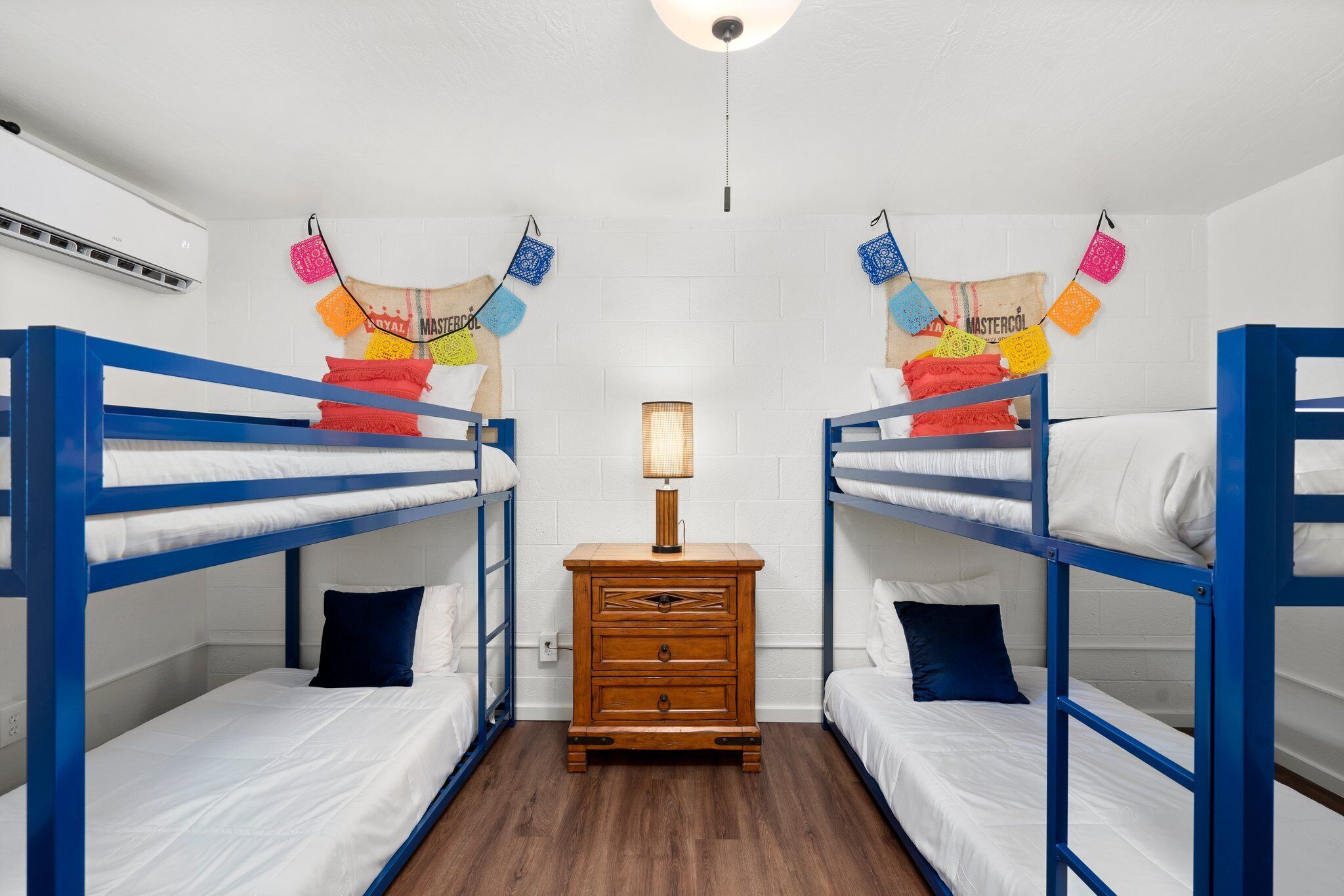 A dormitory room with bunk beds, a wooden dresser, and a wall-mounted lamp.