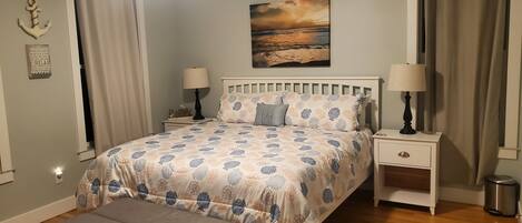 Une chambre à coucher avec un lit, deux tables de chevet, une commode, un banc, un tableau et des rideaux.