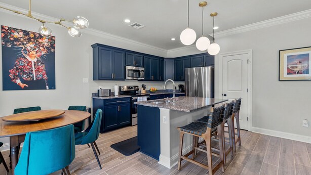 A modern kitchen with dark blue cabinets, stainless steel appliances, and a central island with bar stools.