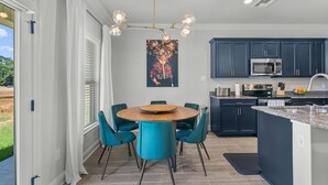 A modern kitchen with dark blue cabinets, a stainless steel microwave, and a round wooden table with teal chairs.