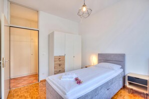 A bedroom with a bed, bedside table, nightstand, wardrobe, and a hanging light fixture.