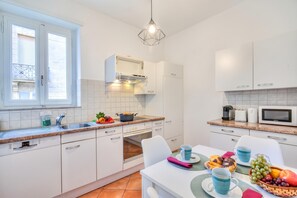 A modern kitchen with white cabinets, a built-in oven, a microwave, and a dining area with a table set for two.