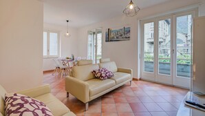 Ein modernes Wohnzimmer mit einem beigefarbenen Sofa, einem gemusterten Kissen und einem Essbereich mit einem weißen Tisch und Stühlen.