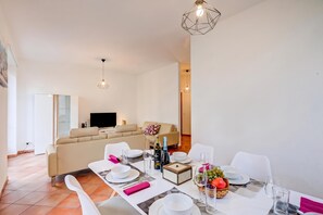A modern dining area with a table set for two, a sofa in the background, and a television on the wall.