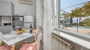 Un coin repas avec une table dressée pour deux personnes, un four à micro-ondes, un saladier de fruits et une bouteille de vin.