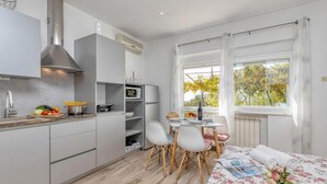 Une cuisine compacte dotée d’appareils électroménagers modernes, un coin repas avec une table et des chaises, et un lit recouvert d’une couvre-lit à motifs floraux.
