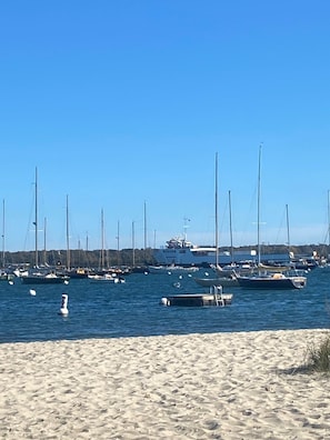 Uma marina com vários veleiros atracados, uma praia de areia e um céu azul e límpido.