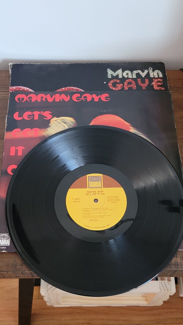Un disque vinyle dont l’étiquette porte les inscriptions « Marvin Gaye » et le titre « Let’s Get It On », interprété par Marvin Gaye, est posé sur une surface en bois.