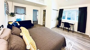 A spacious bedroom with a large bed, a desk, and a window with curtains.