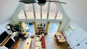 A spacious loft with a high ceiling, large windows, a cozy seating area, a dining table, and a kitchen.