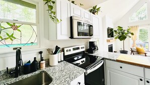 A kitchen with white cabinets, a microwave, a stove, and a sink. There are plants on the cabinets and a window with a stained glass design.