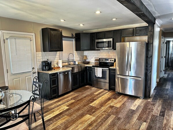 A modern kitchen with dark cabinets, stainless steel appliances, and a herringbone wood floor.