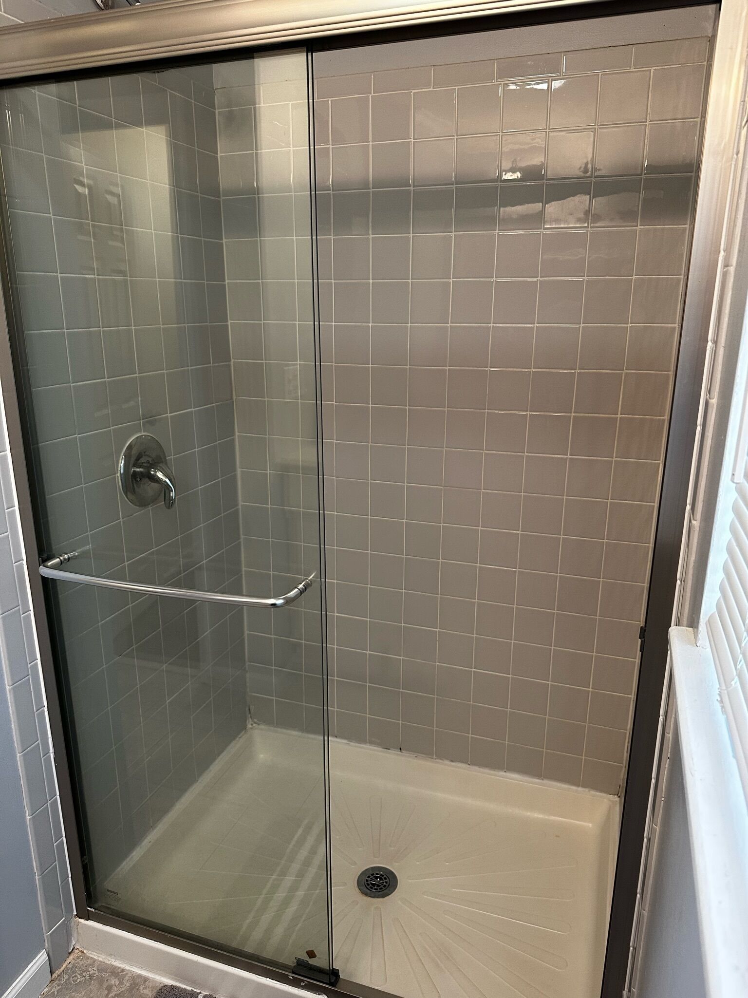 Ducha con cerramiento de vidrio, manija metálica y puerta de cristal.