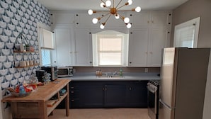 A modern kitchen with white cabinets, a stainless steel refrigerator, a microwave, and a wooden countertop.