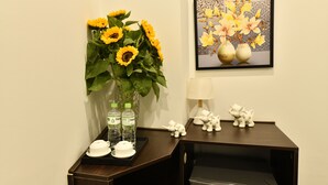A room with a dark wooden desk, a vase with sunflowers, two bottles of water, a framed floral artwork, and a small elephant figurine. - Kingdom Hotel Hanoi (Hanoi)