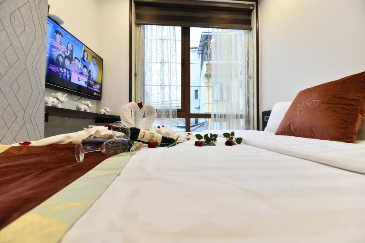 Habitació d'hotel amb un llit, un televisor a la paret i una finestra amb cortines.