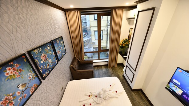 A hotel room with a bed, a TV, a window with curtains, and artwork on the wall. - Kingdom Hotel Hanoi (Hanoi)