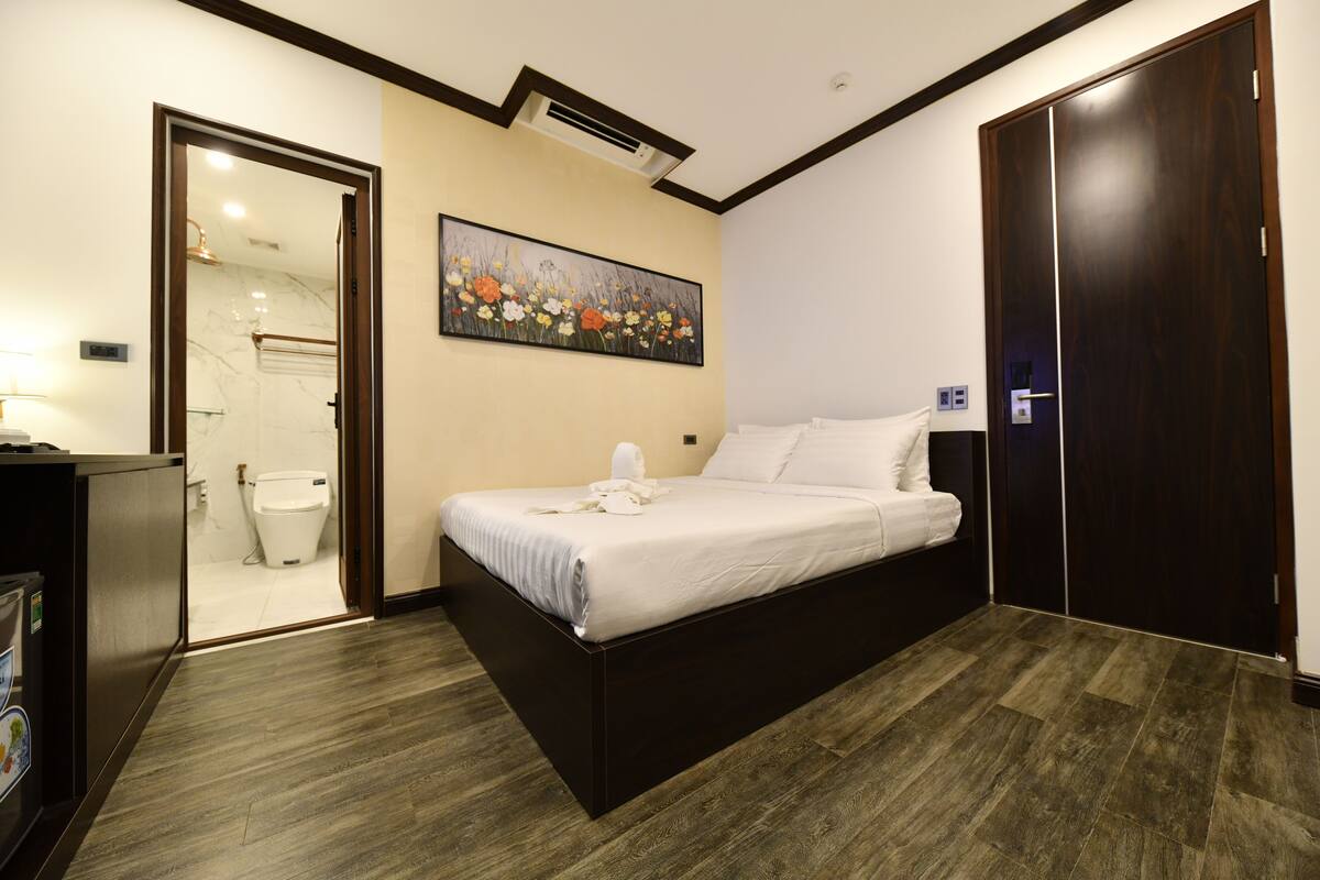 Habitació d'hotel amb un llit, un quadre, un armari i un bany visible a través d'una porta oberta.