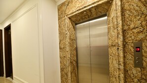 An elevator with a metallic finish, set in a hallway with marble walls and a wooden door. - Kingdom Hotel Hanoi (Hanoi)