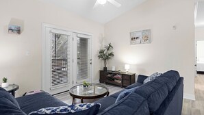 Uma sala de estar com um sofá azul escuro, uma mesa de centro de vidro e um ventilador de teto.