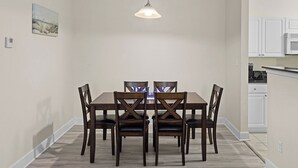 A dining area with a wooden table and chairs, a pendant light, and a kitchen in the background. - Near Tropic Falls Water Park – Fun & Relaxation Await! (Foley)