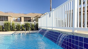 Piscina com borda em azulejos azuis e cerca branca.